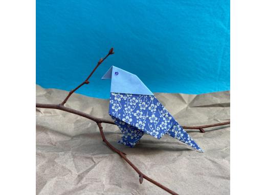 blue bird made from paper. blue paper sky. brown paper ground with delicate tree branch for the paper bird.